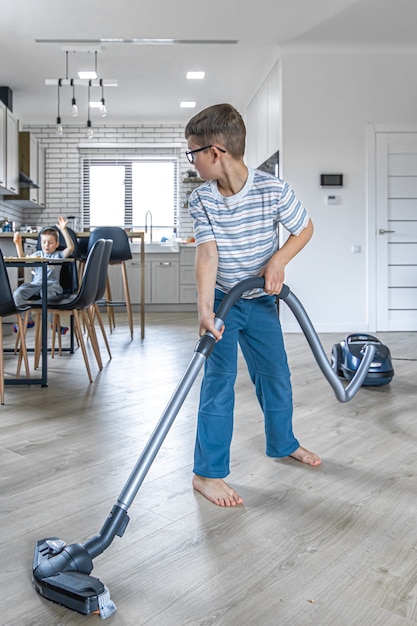 A little boy with glasses cleans the house with a vacuum cleaner.