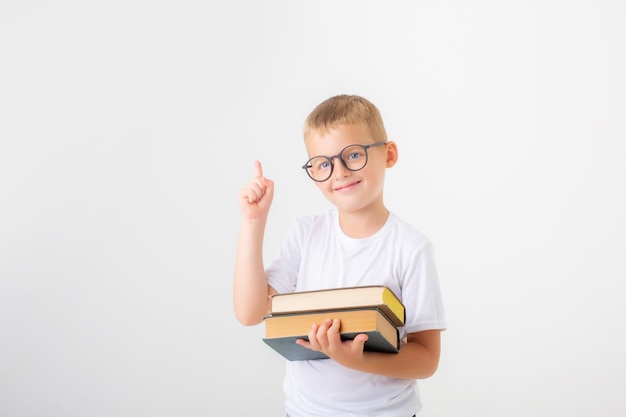 A little boy with glasses holds a stack of books on a white background isolated