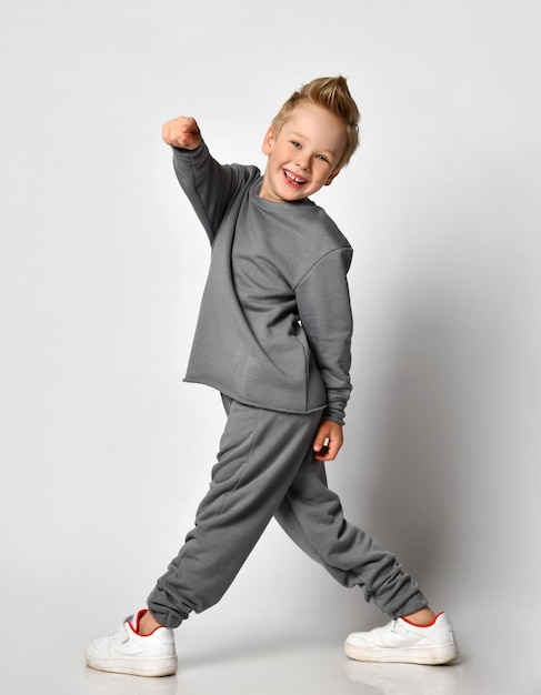 Little boy with a happy smile turning back and pointing his finger at the camera studio shot on a white background Child with European appearance in fashionable sportswear smiles happily