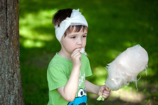 A little boy with a head or ear injury eats cotton candy with pleasure in the park the child received sweets for courage a head injury in the summer in the park