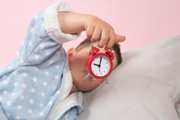 Little boy with a red alarm clock in his hands Morning concept Children39s sleep High quality photo