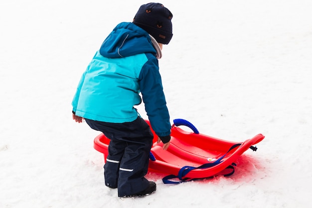 Little boy with red sled in the snow