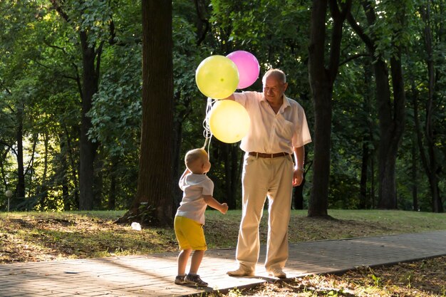 A little boy in yellow shorts and an elderly old man are playing with bright balloons the family is