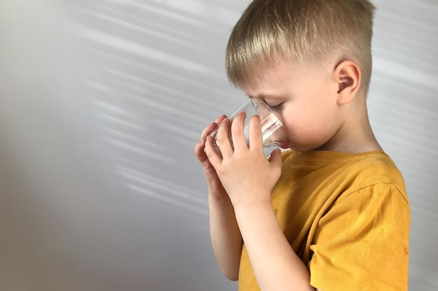 little boy in a yellow Tshirt drinks water