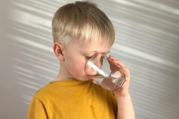 little boy in a yellow Tshirt drinks water