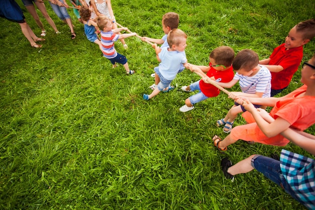 The little boys and girls are playing tug of war in the garden