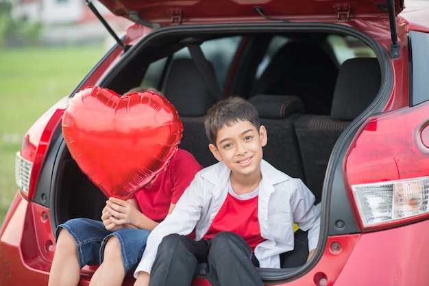 Little boys sitting on the back door of the car with balloon heart in hand