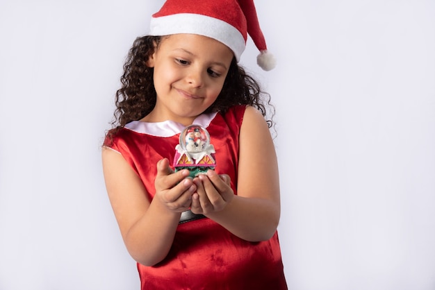 Little Brazilian girl dressed with christmas costume holding snow globe