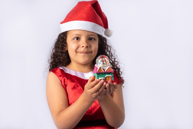 Little Brazilian girl dressed with christmas costume holding snow globe