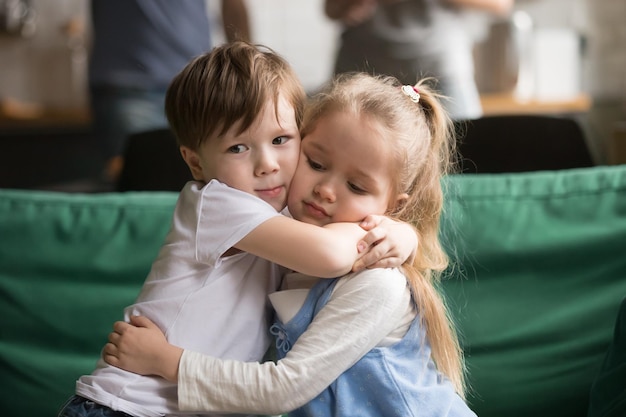 Photo little brother hugging upset sister sitting together on couch at home sincere toddler boy embracing depressed girl apologizing supporting good relationship friendship compassion empathy concept