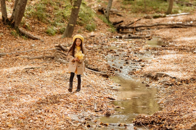 little brunette Asian girl in autumn clothes walks in the autumn forest near a stream