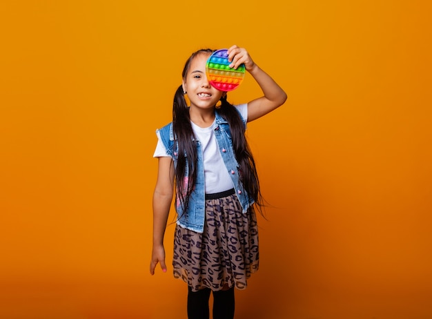 Little brunette girl holding pop it antistress toy on yellow background with place for text