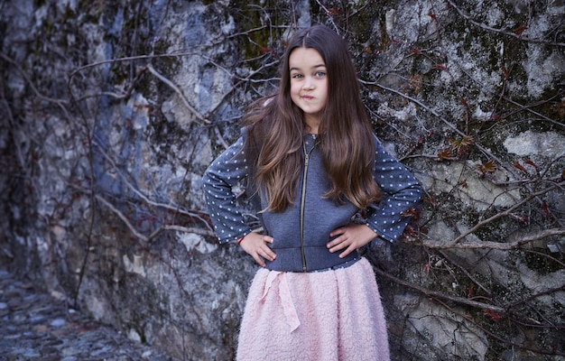 Little brunette girl in a skirt and hoodie on natural grey background.