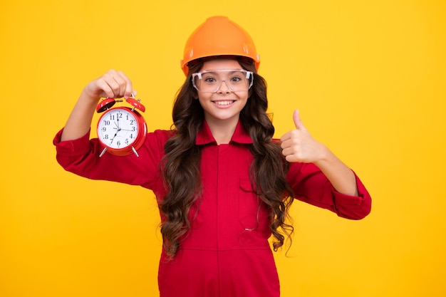 Little builder expert in helmet on construction site Teen girl painter with painting brush tool or paint roller Child on repairing work Renovation concept Happy smiling girl