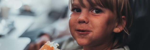 Little candid kid boy five year old eats burger or sandwich food sitting in airplane seat on flight traveling from airport children take a bite child in air plane eating lunch or dinner meal banner