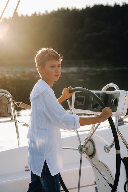 Photo a little captain at the helm on a yacht. a little boy at the helm of the captain on a yacht at sunset.