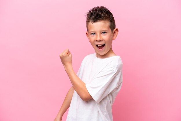 Little caucasian boy isolated on pink background celebrating a victory