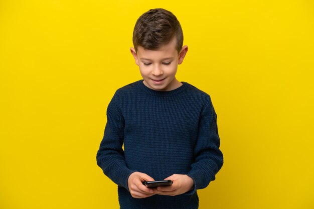 Photo little caucasian boy isolated on yellow background sending a message with the mobile