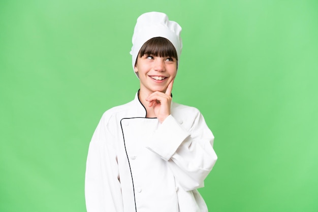 Little caucasian chef girl over isolated background thinking an idea while looking up