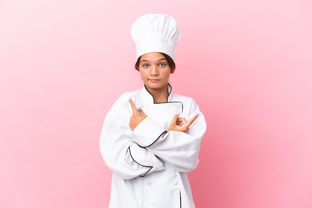 Little caucasian chef girl isolated on pink background pointing to the laterals having doubts