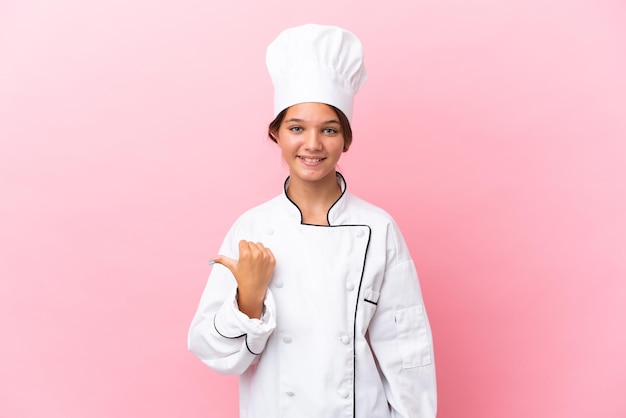 Little caucasian chef girl isolated on pink background pointing to the side to present a product