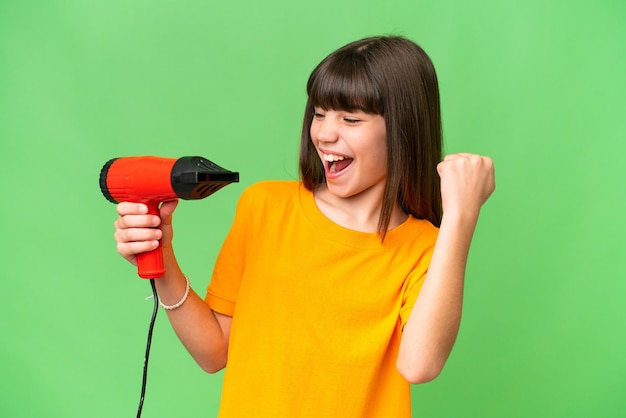 Little Caucasian girl holding a hairdryer over isolated background celebrating a victory