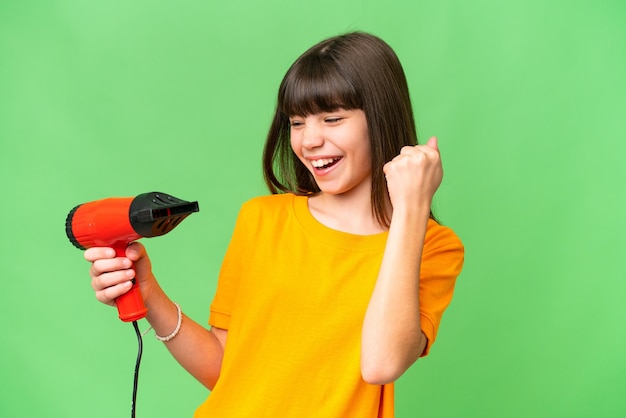 Little Caucasian girl holding a hairdryer over isolated background celebrating a victory