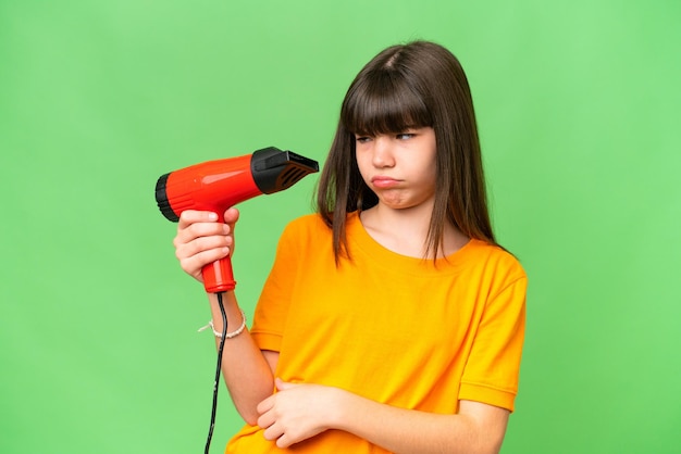 Little Caucasian girl holding a hairdryer over isolated background with sad expression