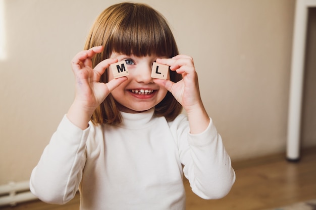 Little Caucasian girl holding wooden letters in front of her face. Early development of child concept.