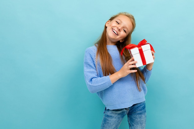 Little caucasian girl holds a white box with gift and has a lot of emotions isolated on blue