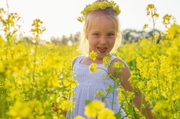 A little caucasian girl is playing on a flowering rape meadow