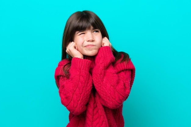 Little caucasian girl isolated on blue background frustrated and covering ears