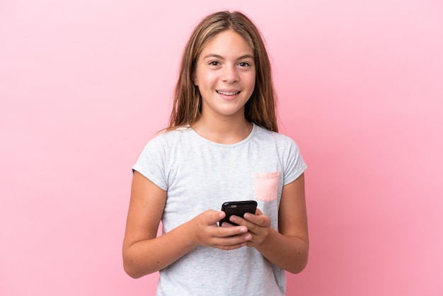 Little caucasian girl isolated on pink background sending a message with the mobile