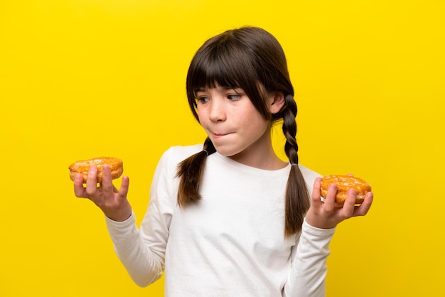 Little caucasian girl isolated on yellow background holding donuts