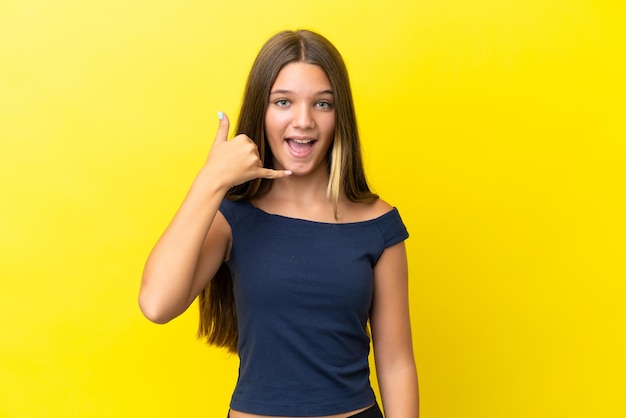 Little caucasian girl isolated on yellow background making phone gesture Call me back sign