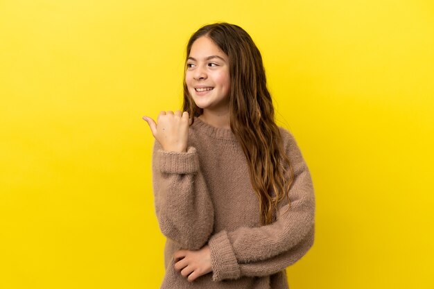 Little caucasian girl isolated on yellow background pointing to the side to present a product