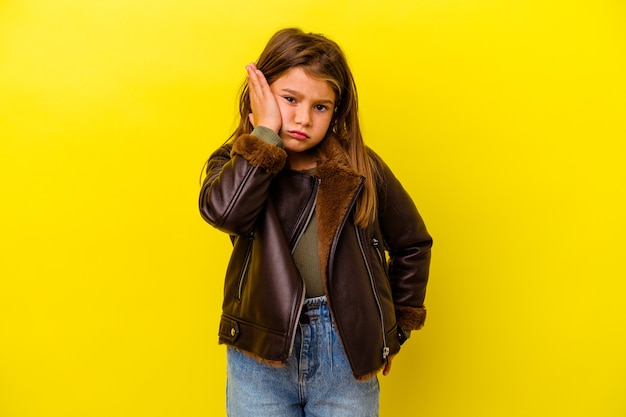 Little caucasian girl isolated on yellow tired and very sleepy keeping hand on head.