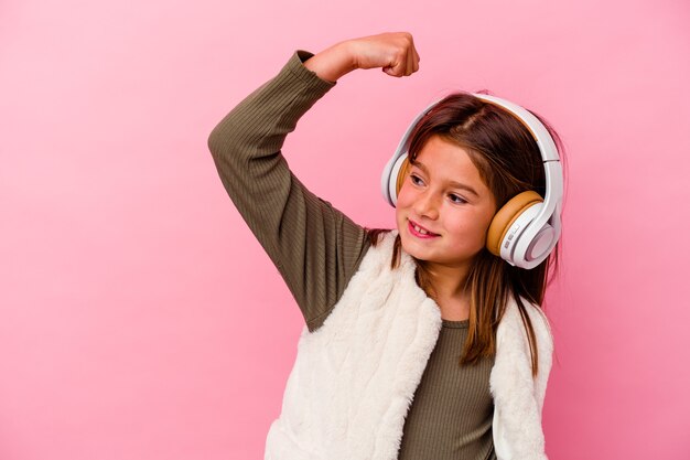 Photo little caucasian girl listening music isolated on pink wall raising fist after a victory, winner concept.