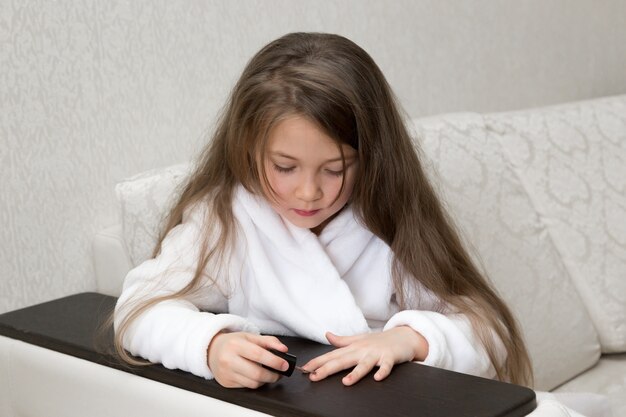 Little Caucasian girl paints nails on hands.