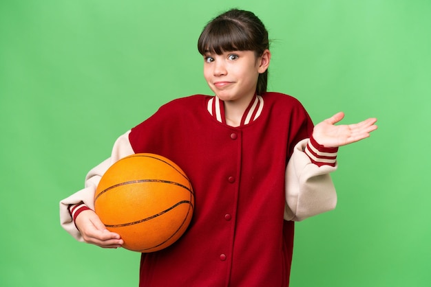 Little caucasian girl playing basketball over isolated background having doubts while raising hands