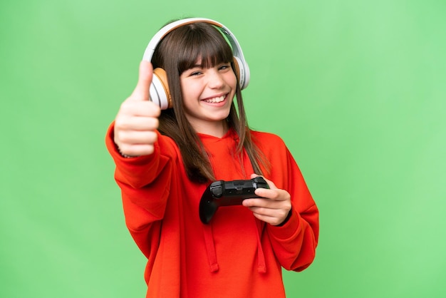 Little caucasian girl playing with a video game controller over isolated background with thumbs up because something good has happened