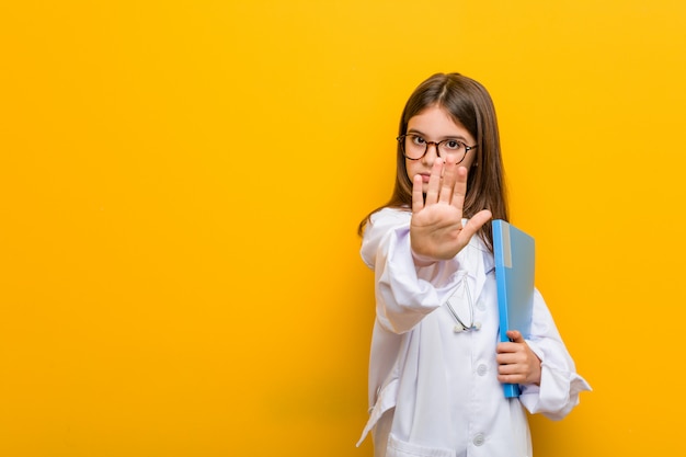 Little caucasian girl wearing a doctor costume looking sideways with doubtful and skeptical expression.