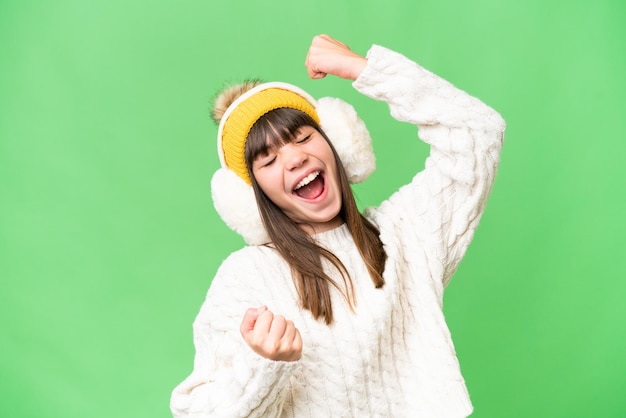 Little caucasian girl wearing winter muffs over isolated background celebrating a victory