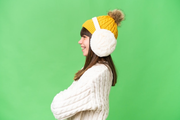 Photo little caucasian girl wearing winter muffs over isolated background in lateral position