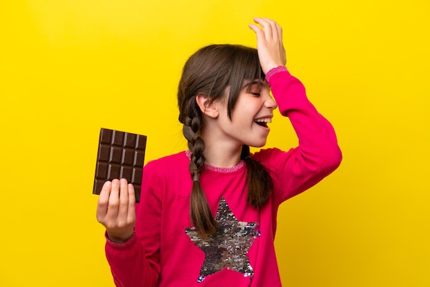 Little caucasian girl with chocolat isolated on yellow background has realized something and intending the solution