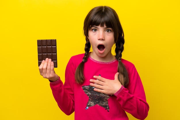 Photo little caucasian girl with chocolat isolated on yellow background surprised and shocked while looking right