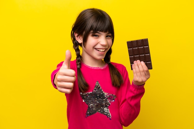 Little caucasian girl with chocolat isolated on yellow background with thumbs up because something good has happened