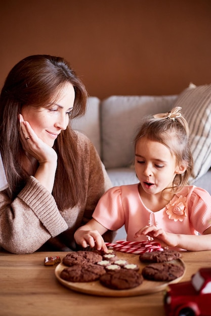 Little caucasian girl with mother eating tasty Christmas cookies Happy family christmas concept