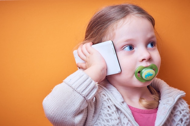 Little Caucasian girl with a phone in her hand on a colored