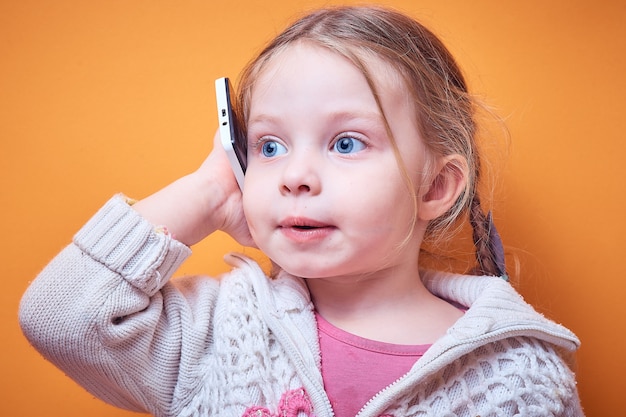 Little Caucasian girl with a phone in her hand on a colored